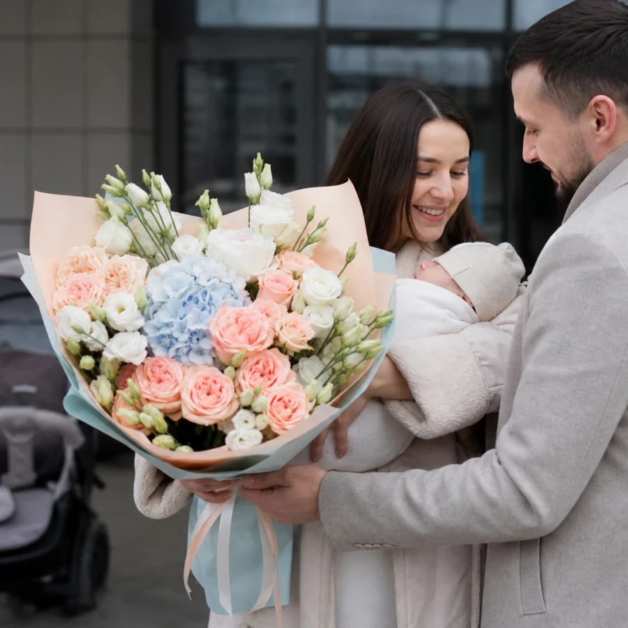 Родители с новорождённым и букетом из персиковых роз и голубой гортензии у роддома
